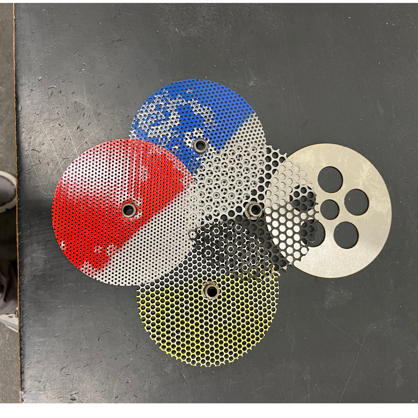 Four circular metal filters with different patterns on a metallic surface